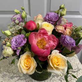 Low mixed bouquet of pink peonies, cream roses, and purple lisianthus in a clear glass vase
