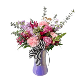 Pink and lavender mixed bouquet in a purple vase with a striped ribbon