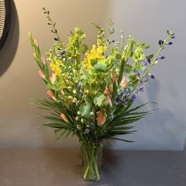 Tall mixed bouquet in a clear glass vase with yellow, purple, and peach blooms