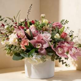 Low arrangement of pink orchids and roses with white and peach blooms in a white ceramic cylinder vase