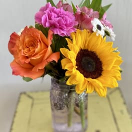 Bouquet of orange roses, pink carnations, and a sunflower in a glass jar