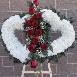 Heart-shaped white floral wreath with red roses on an easel
