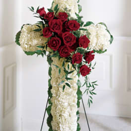 Cross-shaped floral tribute with red roses and white flowers on a stand