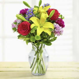 Bouquet of red roses, yellow lilies, and purple flowers in a clear glass vase
