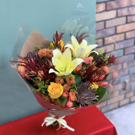 Bouquet of yellow lilies, roses, and mixed blooms wrapped in paper