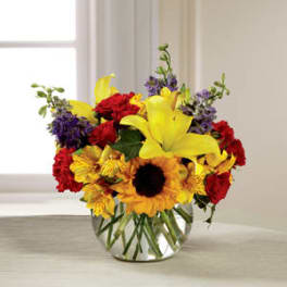 Mixed bouquet with yellow lilies, red roses, and sunflowers in a glass vase