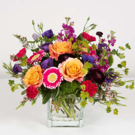 Mixed bouquet of orange, pink, and purple flowers in a clear glass vase