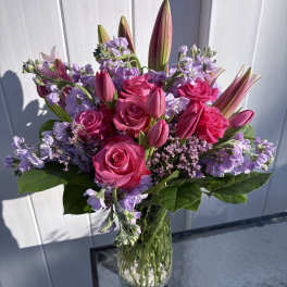Pink roses and lilies arranged in a clear glass vase with lavender flowers