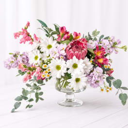 Mixed bouquet in a clear glass pedestal vase with pink, white, and lavender flowers