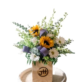 Sunflowers and white daisies arranged in a wooden box with plaid ribbon