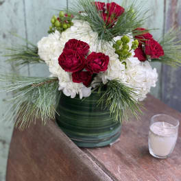 Red roses and white hydrangeas in a green vase with pine accents