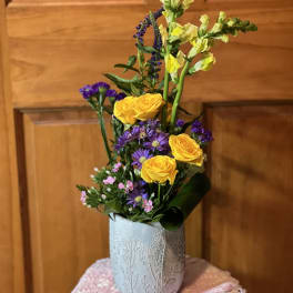 Yellow roses and purple flowers in a patterned vase