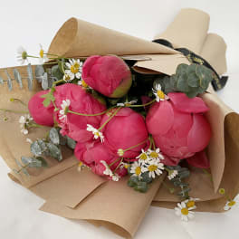 Bouquet of bright pink peonies with small white daisies in brown paper