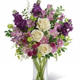 Bouquet of white roses and purple flowers in a clear glass vase