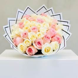 Round bouquet of cream and soft pink roses wrapped in layered white paper with black trim