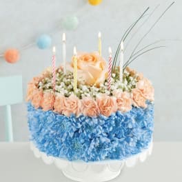 Round floral cake with candles and peach roses on a white stand