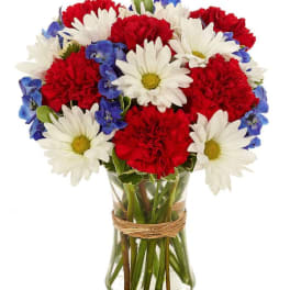 Bouquet of red carnations, white daisies, and blue flowers in a glass vase