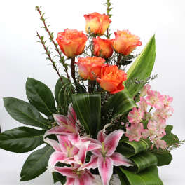 Orange roses and pink lilies arranged in a white vase