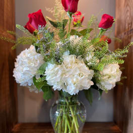 Red roses and white hydrangeas arranged in a clear glass vase