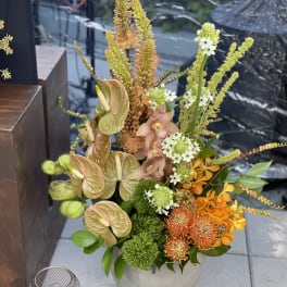 Tall mixed floral arrangement in a gray vase with orange, green, and peach blooms