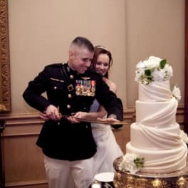 Bride and groom cutting a tall white wedding cake with white flowers
