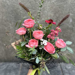 Hand-tied bouquet of pink roses with mixed greenery and small white flowers