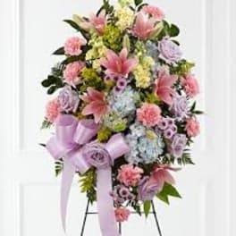 Standing floral spray with pink and lavender blooms and a purple ribbon bow