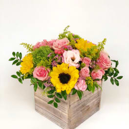 Low wooden box arrangement with yellow sunflowers and pink roses accented by green and purple blooms