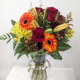 Bouquet of red roses, orange gerbera daisies, and yellow alstroemeria in a glass vase