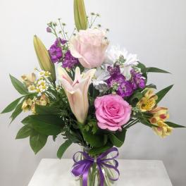 Mixed bouquet of pink roses, lilies, and purple flowers in a glass vase