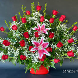 Large arrangement of red roses and pink lilies in a red container