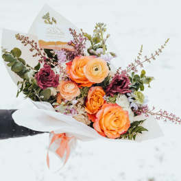 Hand-tied bouquet of orange and yellow roses and ranunculus with burgundy blooms in white wrap