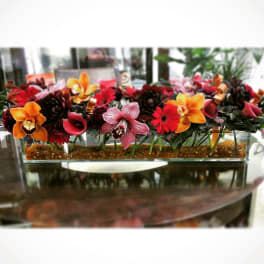 Rectangular floral arrangement with orchids and red blooms in a glass container
