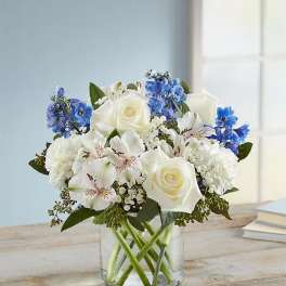 White roses and blue flowers arranged in a clear glass vase