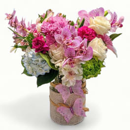 Pink and white mixed flower arrangement in a burlap-wrapped glass vase with pink butterfly accents