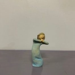 Small figurine of a child in a blue dress with arms crossed