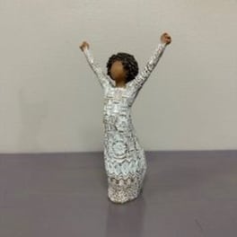 Small decorative figurine of a person with raised arms in a patterned dress