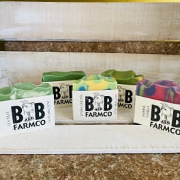 Five bars of colorful goat milk soap on a rustic shelf