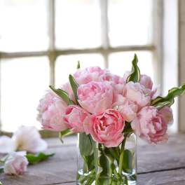 Pink peonies in a clear glass vase on a wooden table