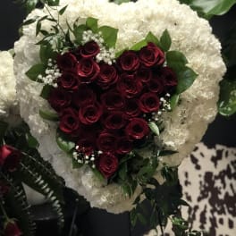 Heart-shaped bouquet of red roses framed by white flowers and greenery