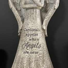 Angel figurine holding a red cardinal with yellow flowers at the base