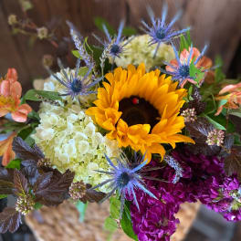Bright mixed arrangement with sunflower, white hydrangea, purple blooms, and blue thistle-like flowers