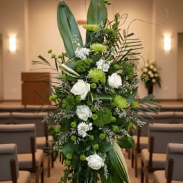 Tall green and white standing spray with roses and mums on a metal easel in a chapel