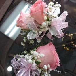 Two pink rose boutonnieres with baby's breath and ribbon bows
