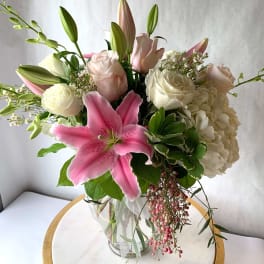 Pink lily, white hydrangea, and pale roses arranged in a clear glass vase