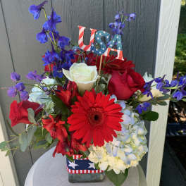 Red, white, and blue flower arrangement in a glass vase with a USA pick