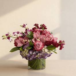 Low arrangement of pink roses and orchids with purple hydrangea in a leaf-lined glass vase