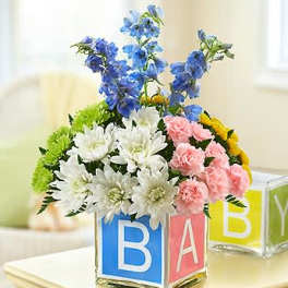 Colorful flower arrangement in alphabet blocks with blue, white, pink, and yellow blooms