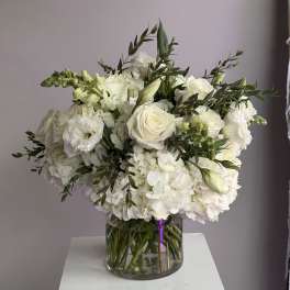 Round arrangement of white roses, hydrangeas, and other white blooms in a clear glass vase