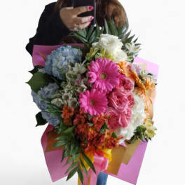 Large mixed bouquet of pink gerbera daisies, roses, hydrangeas and other flowers wrapped in pink and gold paper